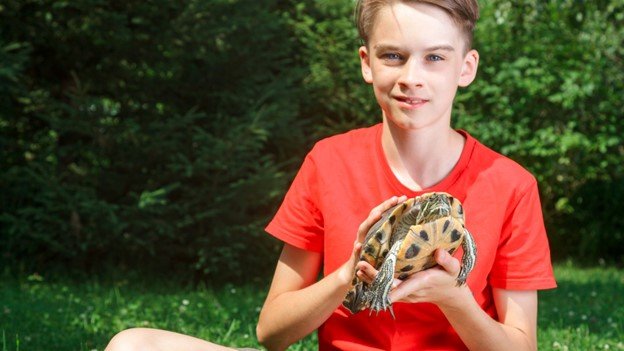 a young boy caring his pet turtle